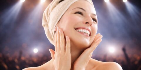 Žena dodiruje lice ispred zamućene koncertne pozadine sa svjetlima reflektora kao ilustracija njege kože prije koncerta