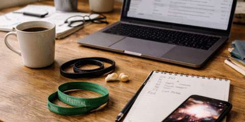 Radni stol nekoliko dana nakon koncerta s laptopom, bilježnicom, kavom, čepićima za uši i koncertnom narukvicom